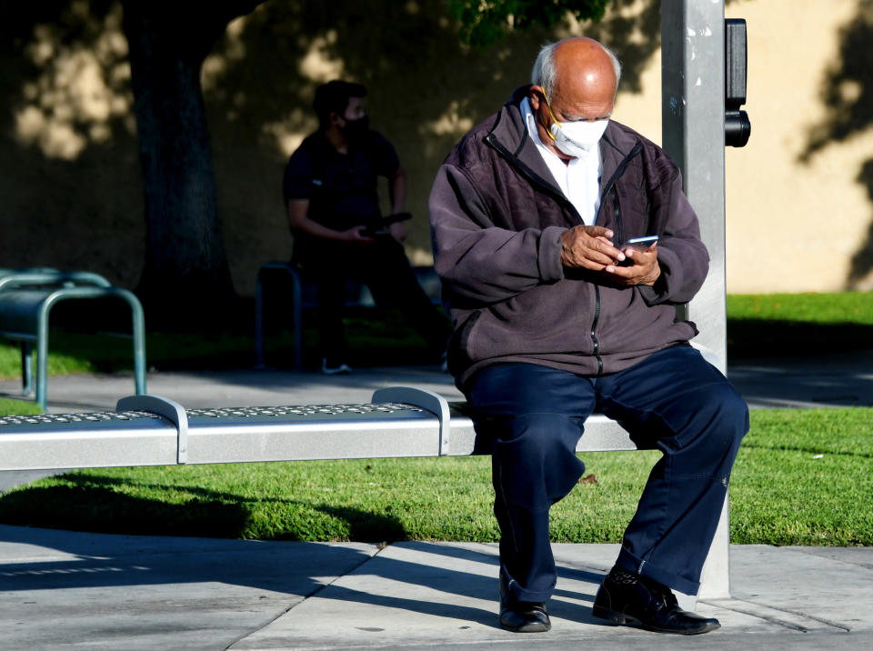 BELL, CA - APRIL 14:  A man wearing a mask during to the Coronavirus Pandemic waits looks at his phone as he waits for a bus along Atlantic Ave. in Bell on Tuesday, April 14, 2020. (Photo by Keith Birmingham/MediaNews Group/Pasadena Star-News via Getty Images)