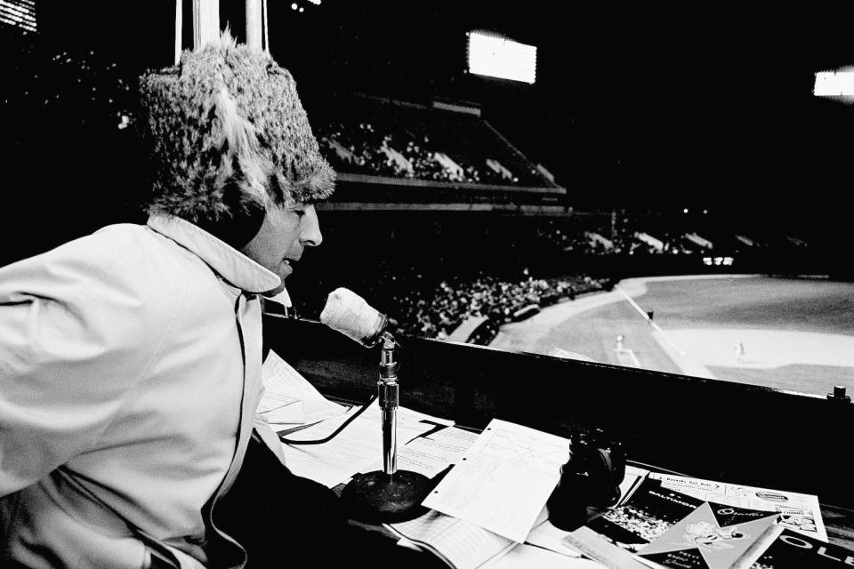 FILE - Former New York Yankee baseball star Phil Rizzuto, who played in games during cooler weather, took no chances as he broadcast Baltimore-New York game from the radio booth in Baltimore, Md., April 18, 1962. Many baseball fans, especially older ones, originally fell in love with America’s pastime by listening to ballgames on AM radio. But several major automakers are eliminating broadcast AM radio from newer models, prompting lawmakers on Capitol Hill to propose legislation that would prevent the practice for safety and other reasons. (AP Photo/File)