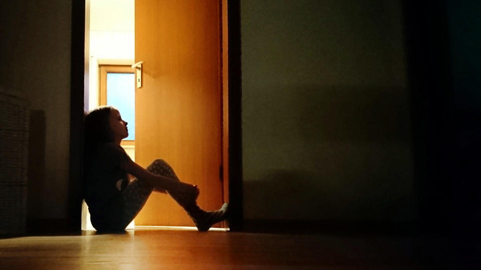 Backlit child sitting in a dark doorway in contemplation