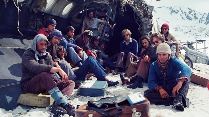 The survivors huddle around in the wreckage of the plane in a still from Society of the Snow