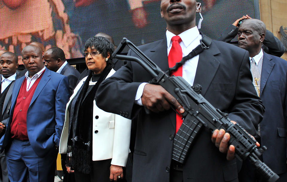 <p>The youth leader of South Africa’s ruling party, Julius Malema, second from left, and former wife of South African icon Nelson Mandela, Winnie Madikizela-Mandela, stand next to an armed bodyguard, outside the court in Johannesburg on April 21, 2011. Malema said that singing “Shoot the Farmer” does not incite violence during a hate speech trial that has captivated the nation. Afriforum, a lobby that sees itself as the voice of white Afrikaners, wants the song banned as hate speech in its suit against Malema. (Photo: Alexander Joe/AFP/Getty Images) </p>