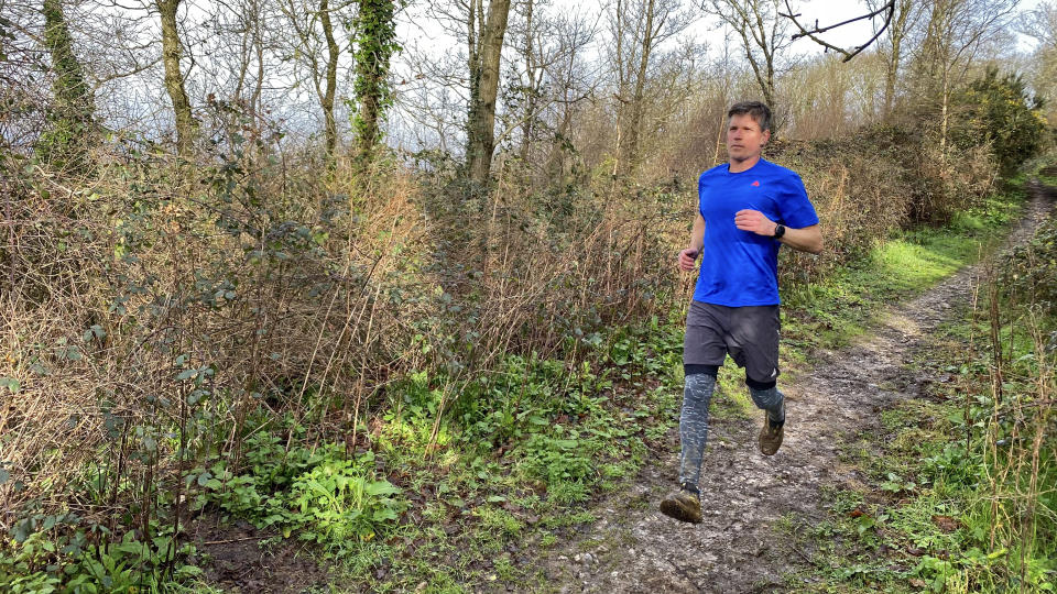 A man wearing Saxx Roast Master Mid-Weight Tights runs along a woody trail.