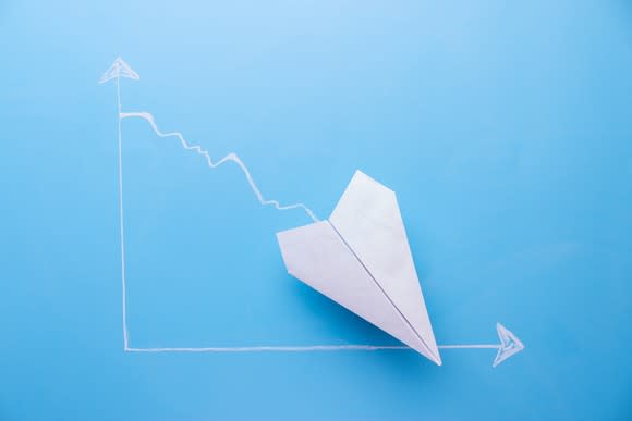 White paper airplane pointing about 45 degree downward on a blue graph background.