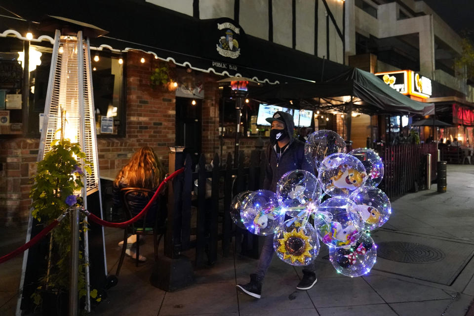 A street vendor walks past Ye Olde King's Head on Thursday, Nov. 19, 2020, in Santa Monica, Calif. The British restaurant and bar in seaside Southern California has been battered the past nine months and was in the process of adapting to new restrictions that took effect Friday, Nov. 20 that would further crimp its recovery even as the prospect of a stay-home order loomed that could cripple the business. (AP Photo/Marcio Jose Sanchez)