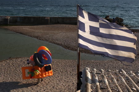 A beach vendor walks on the beach while a Greek flag flutters at a southern Athens suburb July 30, 2015. REUTERS/Yiannis Kourtoglou