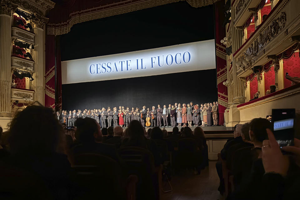 La Scala's dance company and the orchestra stand on stage before the final performance of the opera-ballet "Madina" beneath a banner reading: "Ceasefire" in Milan, Italy, Saturday March 9, 2024. The sentiment received a standing ovation lasting at least two minutes Saturday evening before the final performance of the opera house's original production “Madina,” which tells the story of a Chechen woman who is manipulated to become a suicide bomber after she is orphaned and raped by Russian soldiers. (AP Photo/Colleen Barry)