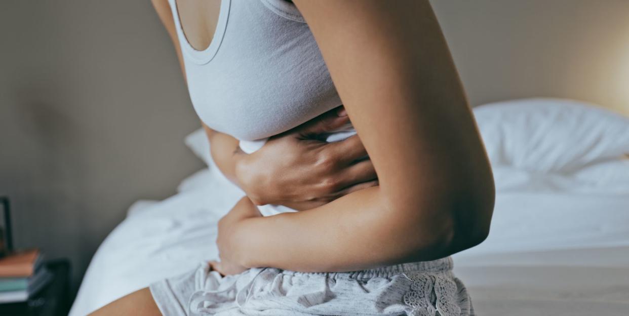 woman holding stomach due to ache, sitting in bed