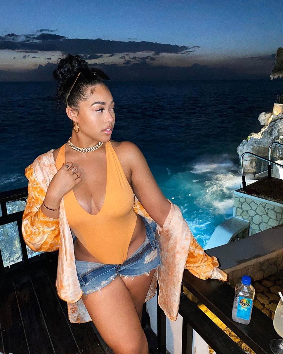 Jordyn Woods poses in a swimsuit and Daisy Dukes