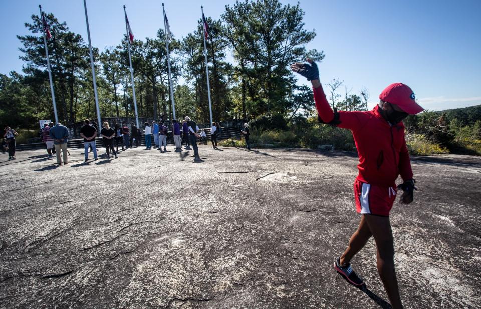 FILE-In this Tuesday, Oct. 6, 2020 file photo, a man with his hand raised walks in circles as a prayer is delivered to attendees at the base of Stone Mountain, in Stone Mountain, Ga. The board overseeing an Atlanta area park that has centuries-old ties to the Ku Klux Klan and contains the largest Confederate monument ever crafted will be headed for the first time by an African American, Rev. Abraham Mosley. (AP Photo/Ron Harris, File)