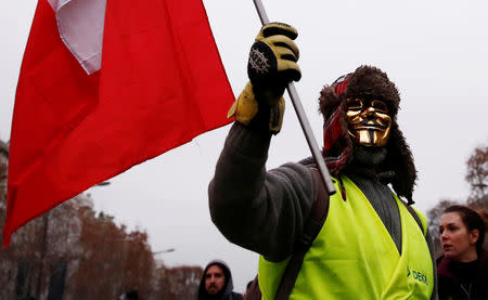 A protester holding a French flag and wearing a Guy Fawkes mask takes part in a demonstration by the "yellow vests" movement on the Champs Elysees near the Arc de Triomphe in Paris, France, December 29, 2018. REUTERS/Christian Hartmann