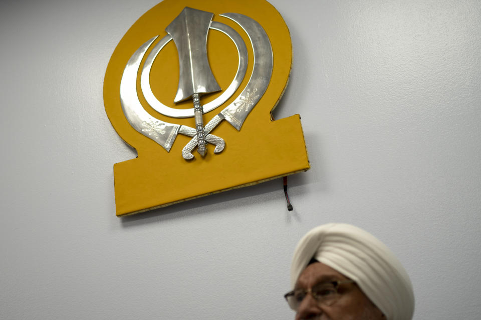 Paramjit Singh Bedi, co-chair of Guru Nanak Darbar of Long Island, a Sikh gurudwara, sits below the Khanda, the symbol of the Sikh faith, Wednesday, Aug. 24, 2022, in Hicksville, N.Y. An Afghan Sikh family of 13 has found refuge in the diaspora community on Long Island where the Sikh community is helping family members obtain work permits, housing, healthcare and find schools for the children. (AP Photo/John Minchillo)