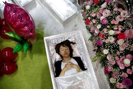 A staff lies in a casket next an altar decorated with flowers and balloons as she demonstrates Okuribito funeral's funeral service at the Life Ending Industry Expo in Tokyo, Japan, August 22, 2016. REUTERS/Kim Kyung-Hoon