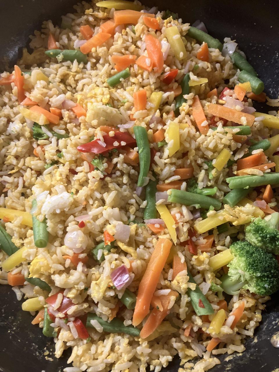 A close-up view of a pan filled with mixed vegetable fried rice, including green beans, carrots, broccoli, and scrambled eggs