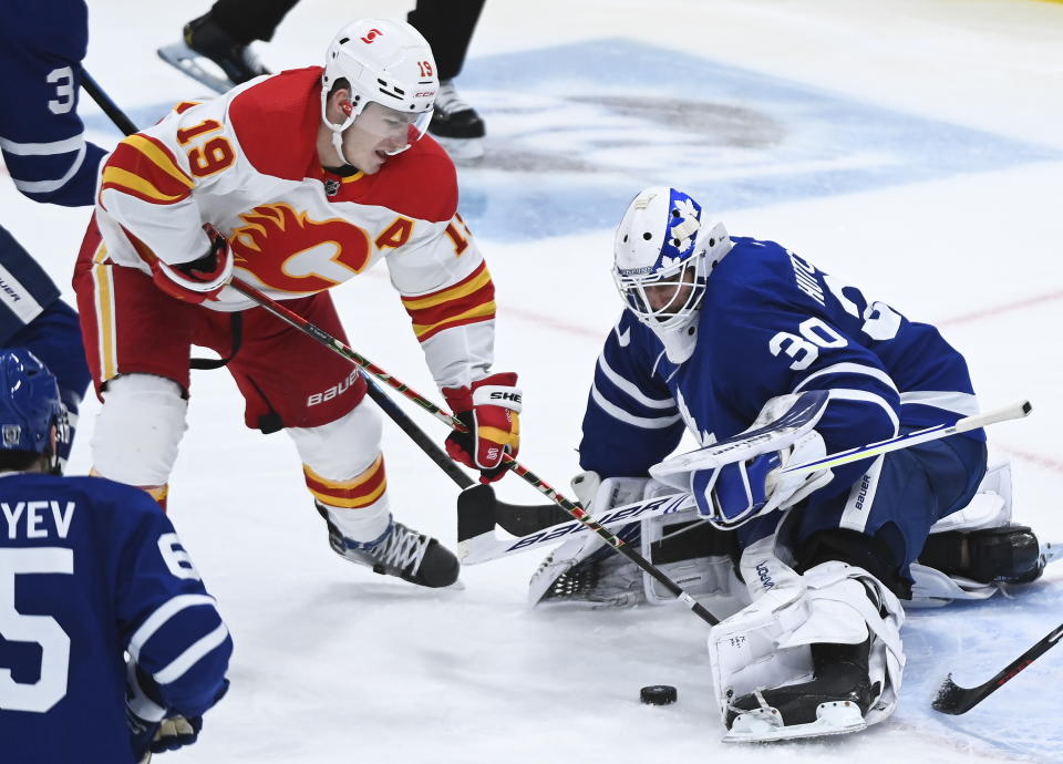 Toronto Maple Leafs goaltender Michael Hutchinson (30) makes a save as Calgary Flames left wing Matthew Tkachuk (19) digs out the rebound during the third period of an NHL hockey game in Toronto on Monday, Feb. 22, 2021. (Nathan Denette/The Canadian Press via AP)