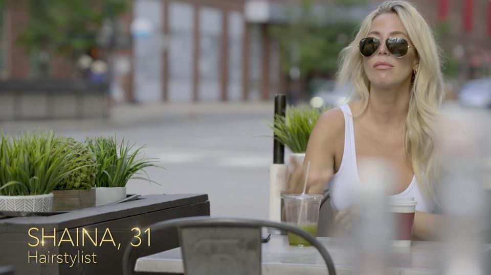 Shaina sitting in sunglasses outside drinking a green juice