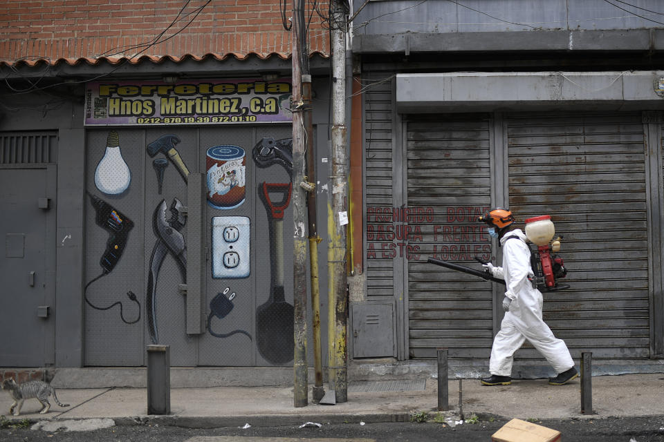 A city worker sprays disinfectant on shuttered storefronts in the Catia neighborhood of Caracas, Venezuela, Saturday, Aug. 8, 2020, amid the new coronavirus pandemic. (AP Photo/Matias Delacroix)