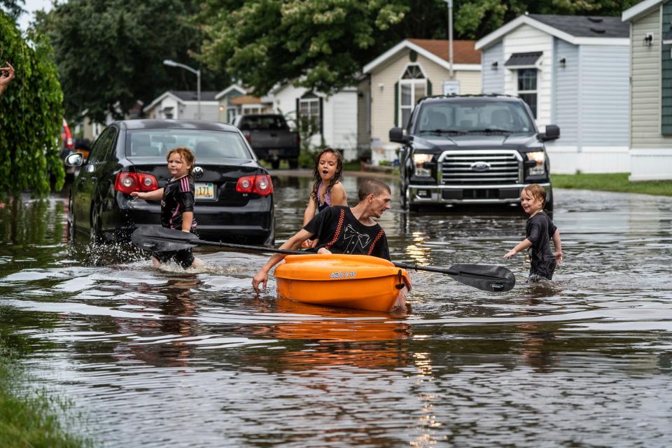 Todd Meggison sits in a kayak as his nephews Keith Carter, daughter Karen Meggison and nephew Carter Meggison play in the water through a section of flooded roadway on Hickory in the Maple Leaf North mobile home park in Canton on Thursday, Aug. 24, 2023, after heavy rains brought flooding to multiple communities.