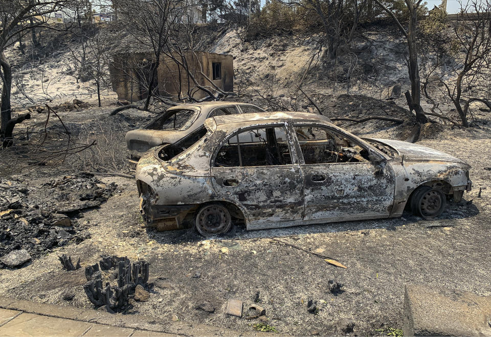 The gutted remains of cars lie on a road after a forest fire, on the island of Rhodes, Greece, Sunday, July 23, 2023. Some 19,000 people have been evacuated from the Greek island of Rhodes as wildfires continued burning for a sixth day on three fronts, Greek authorities said on Sunday. (Lefteris Diamanidis/InTime News via AP)