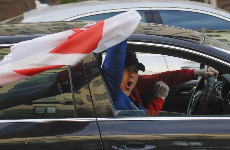 A man waves a flag from a window of a car during a protest rally against the removal of opposition candidates from the presidential elections in Minsk, Belarus, Tuesday July 14, 2020. Election authorities in Belarus on Tuesday barred two main rivals of authoritarian leader Alexander Lukashenko from running in this summer's presidential election. (AP Photo/Sergei Grits)