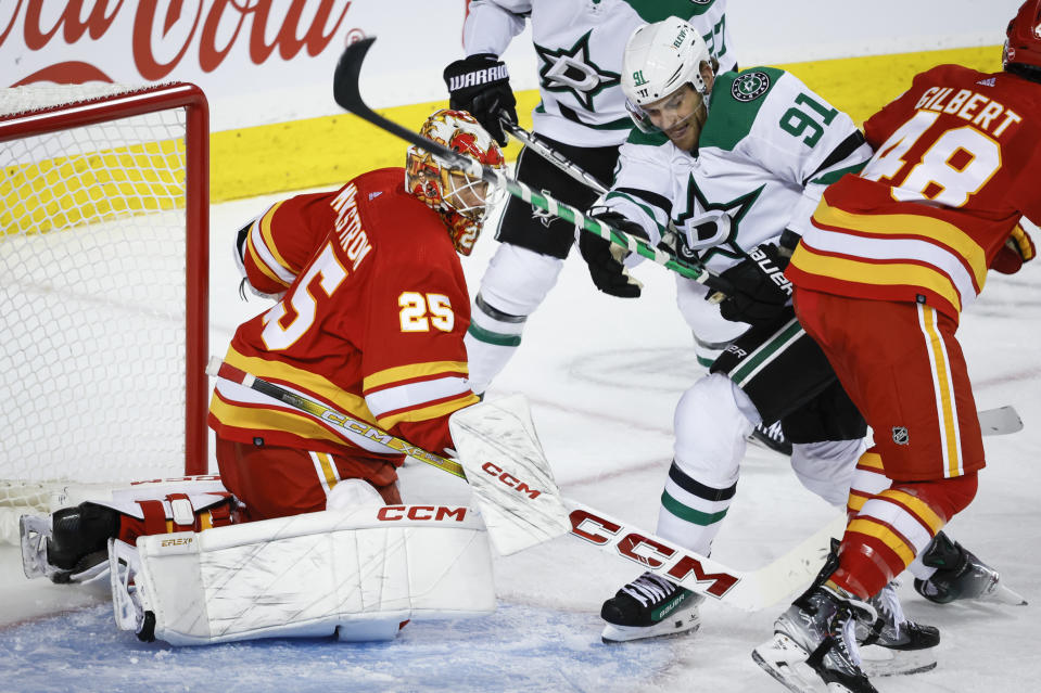 Dallas Stars forward Tyler Seguin, center, is checked by Calgary Flames defenseman Dennis Gilbert, right, as goalie Jacob Markstrom looks on during the second period of an NHL hockey game, Wednesday, Nov. 1, 2023 in Calgary, Alberta. (Jeff McIntosh/The Canadian Press via AP)