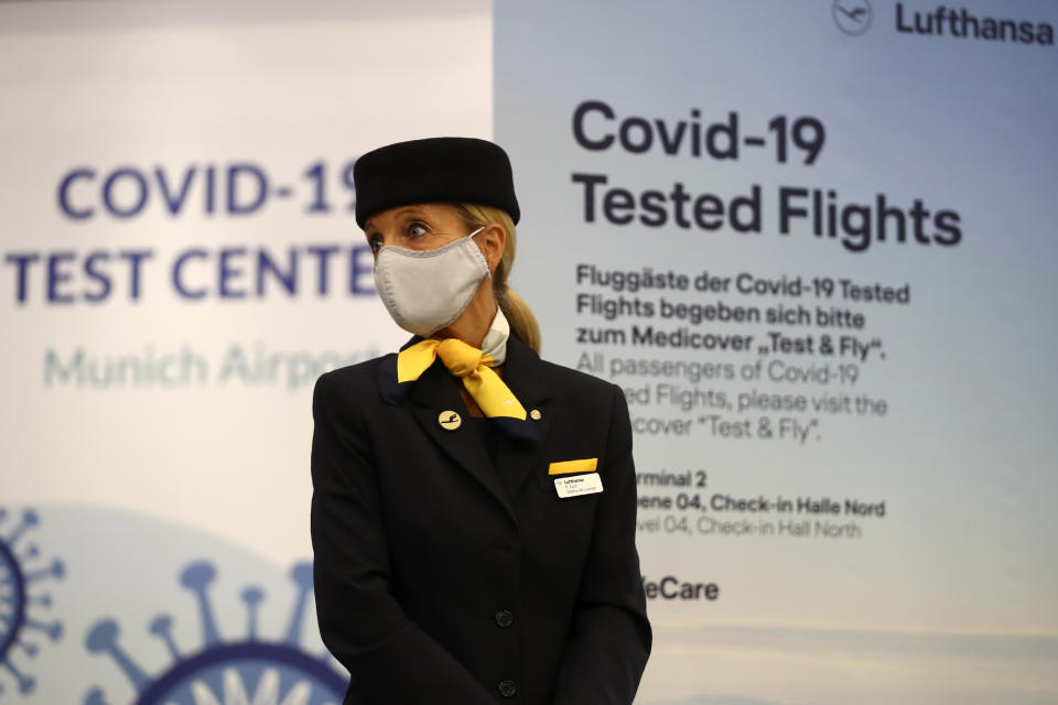 A flight attendant stands in front of the entrance of a new Lufthansa corona quick test center at the airport in Munich, Germany, Thursday, Nov. 12, 2020. Lufthansa starts the first test runs for comprehensive Covid-19 antigen rapid tests on selected routes between Munich and Hamburg. (AP Photo/Matthias Schrader)