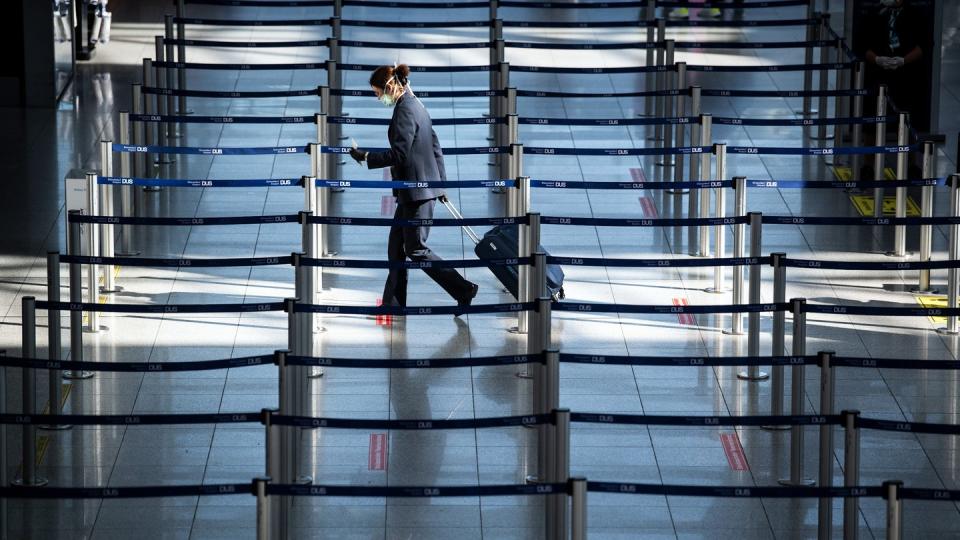 Eine Frau mit Mundschutz geht am Flughafen zu einem Check In-Schalter.