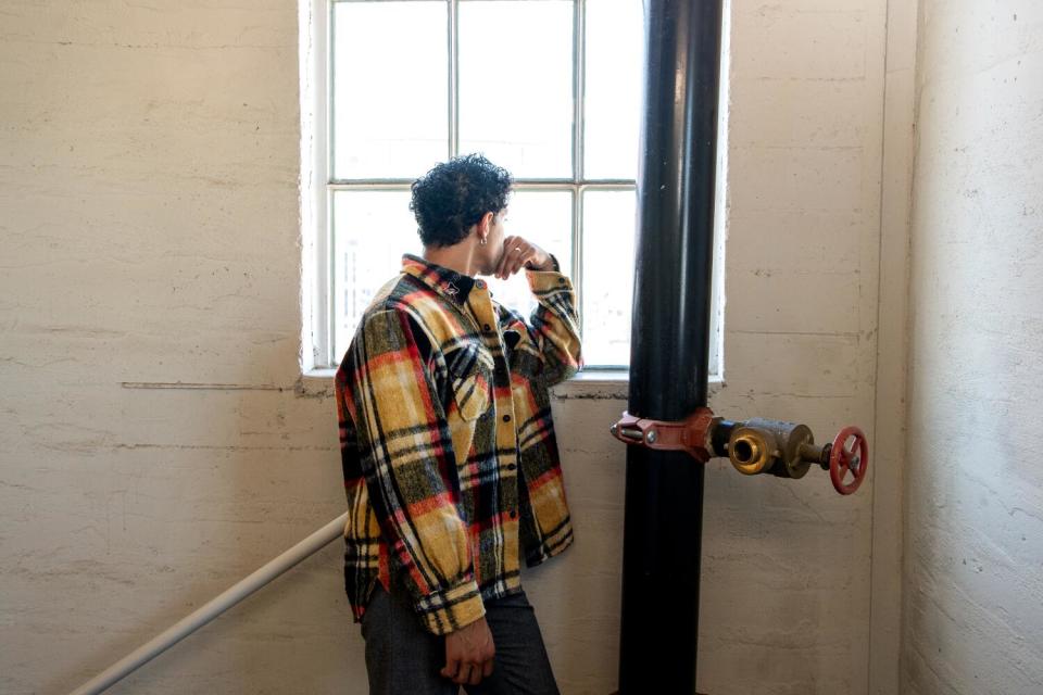 A man stands in a stairwell wearing a plaid yellow, green, and red jacket.