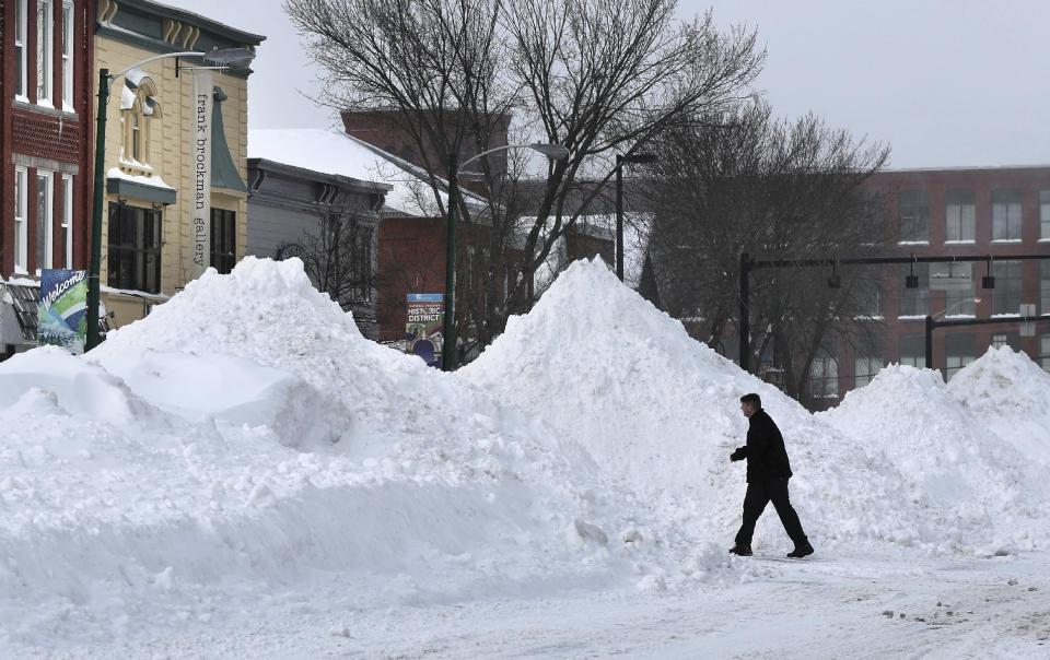 A man crosses Maine Street where snow has been piled high during a blizzard, Monday, Feb. 13, 2017, in Brunswick, Maine. A fluffy snow up to two-feet deep blanketed parts of the Northeast, just days after the biggest storm of the season dumped up to 19 inches of snow on the region. (AP Photo/Robert F. Bukaty)