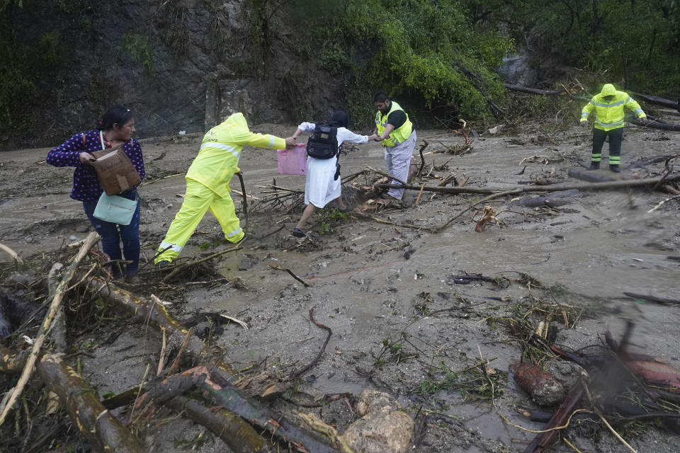 People are helped as they cross a highway blocked by a landslide triggered by Hurricane Otis near Acapulco, Mexico, Wednesday, Oct. 25, 2023. (AP Photo/Marco Ugarte)