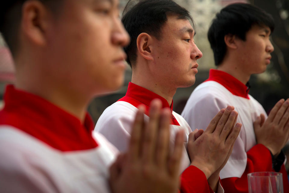 FILE - In this Saturday, March 31, 2018, file photo, Chinese acolytes pray during a Holy Saturday Mass on the evening before Easter at the Cathedral of the Immaculate Conception, a government-sanctioned Catholic church in Beijing. A southern Chinese city is offering cash rewards for information about "illegal religious groups" as the ruling Communist Party continues to tighten its grip over faith communities. (AP Photo/Mark Schiefelbein, File)