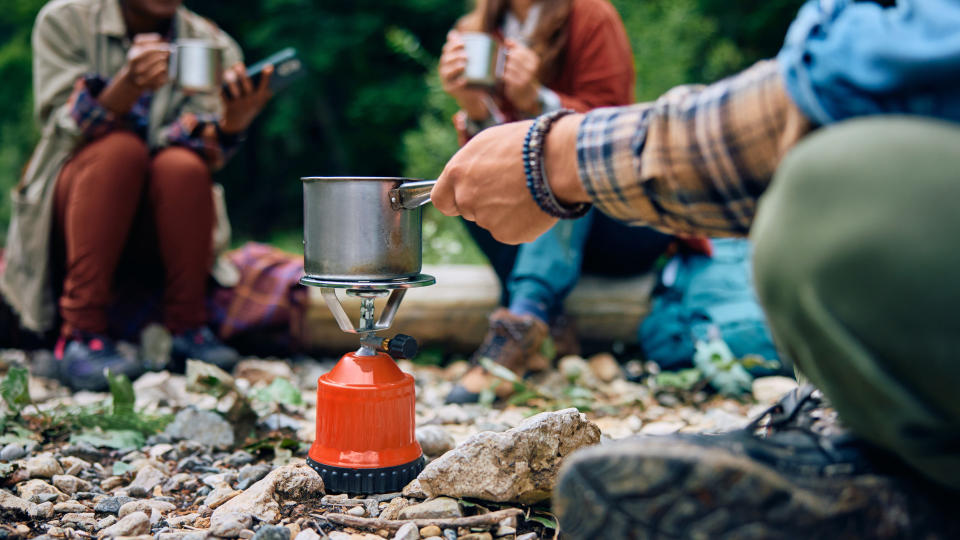     A group of campers boil water on a camping stove. 