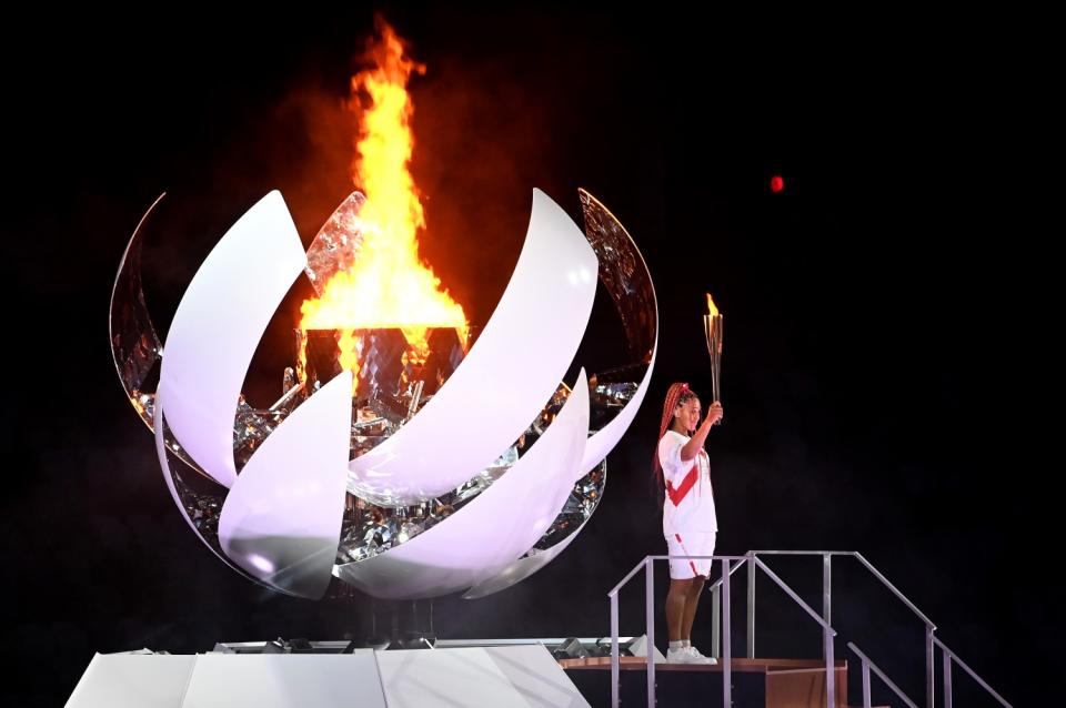 A woman stands atop a platform holding a torch