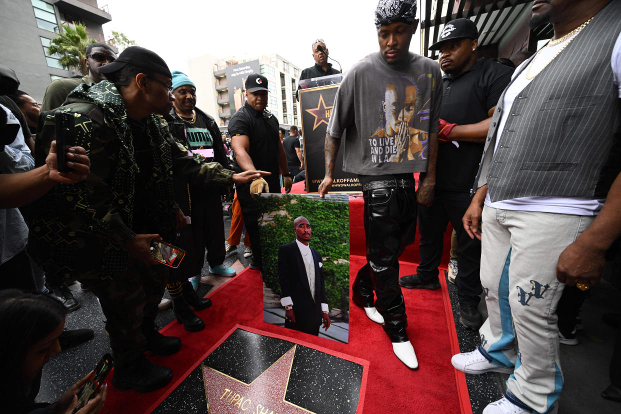 A group of men gather around a Hollywood Walk of Fame star ensconced by red carpet. They are holding a portrait of the late U.S. rapper Tupac Shakur. (Robyn Beck / AFP via Getty Images)