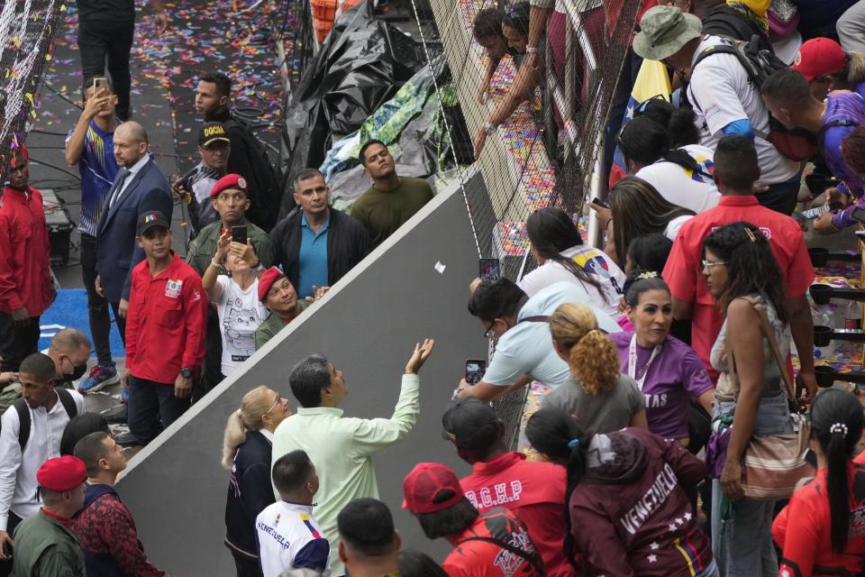 Venezuela's President Nicolas Maduro holds out his hand to catch a paper message thrown down from a supporter as he leaves the Alba Games' opening ceremony, at the baseball stadium in La Guaira, Venezuela, Friday, April 21, 2023. (AP Photo/Ariana Cubillos)