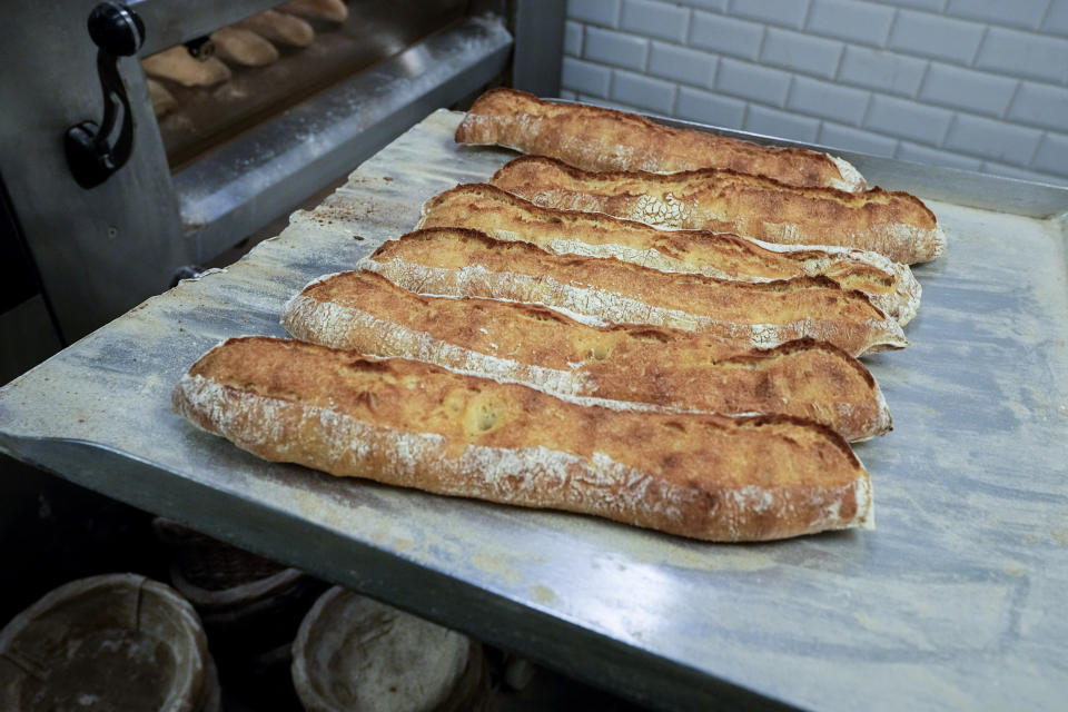 Baguettes are removed from the oven at Feru bakery in Louveciennes, west of Paris, Tuesday, Oct. 26, 2021. A worldwide increase in wheat prices after bad harvests in Russia is forcing French bakers to raise the price of that staple of life in France the baguette. Boulangeries around France have begun putting up signs warning their customers of an increase in the price of their favorite bread due to rising costs. (AP Photo/Michel Euler