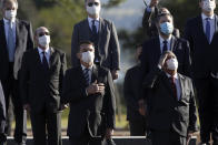 Brazil's President Jair Bolsonaro, with hand on chest, attends a flag raising ceremony with his ministers outside Alvorada palace, the presidential residence in Brasilia, Brazil, Tuesday, May 12, 2020. The morning ceremony flew Brazil's flag at half mast to mourn those who have died from the new coronavirus. (AP Photo/Eraldo Peres)