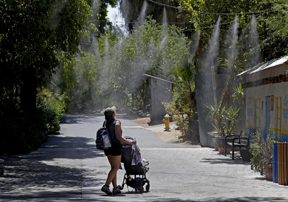 Visitors keep cool under misters at the Phoenix Zoo, Tuesday, July 16, 2019, in Phoenix. The National Weather Service has issued an excessive heat warning to take effect until Wednesday night. The Phoenix Zoo uses spraying, frozen treats and shaded area's to keep their animals cool. (AP Photo/Matt York)