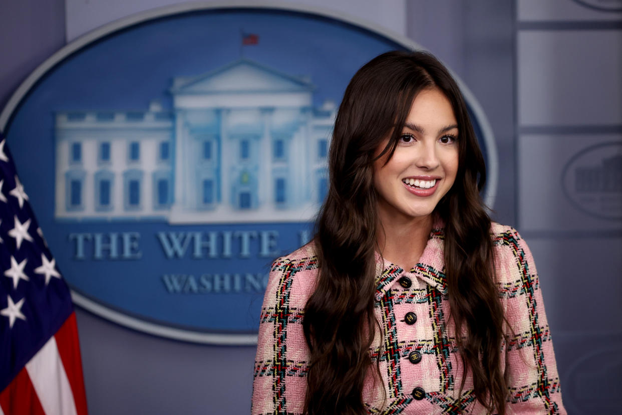 Olivia Rodrigo stands next to an American flag in front of a White House seal