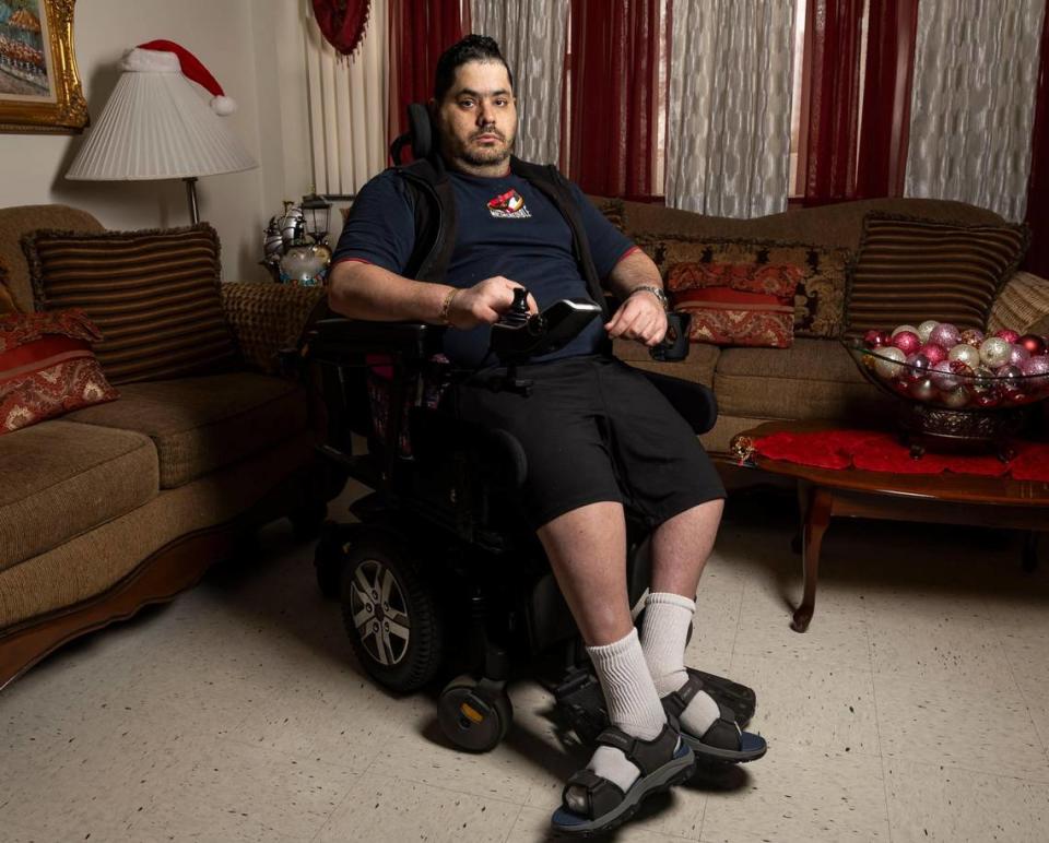 Rudens Rodríguez sits in his electric wheelchair in the living room of his apartment. He bought the wheelchair used several years ago, and it is wearing out.