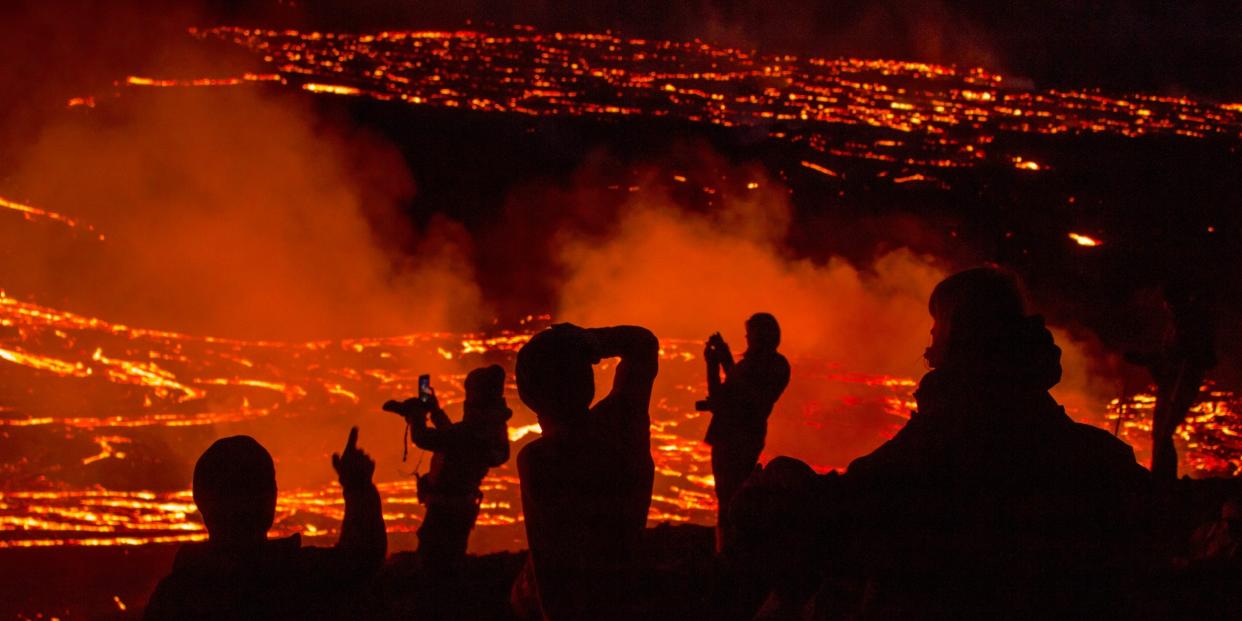 People watch as lava flows from an eruption of a volcano on the Reykjanes Peninsula in southwestern Iceland late on Monday, March 29, 2021.