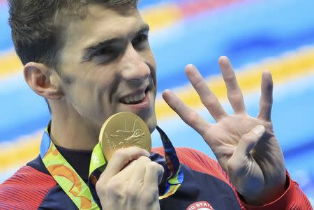 2016 Rio Olympics - Swimming - Victory Ceremony - Men's 200m Individual Medley Victory Ceremony - Olympic Aquatics Stadium - Rio de Janeiro, Brazil - 11/08/2016. Michael Phelps (USA) of USA gestures to indicate the four gold medals he has won at this Olympic games as he poses with his gold medal. REUTERS/Dominic Ebenbichler
