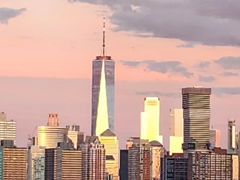 <p>A picture taken with the Galaxy Z Flip 4 showing the World Trade Center and some surrounding buildings zoomed in front a distance at sunset with pink and blue hues in the sky.</p>
