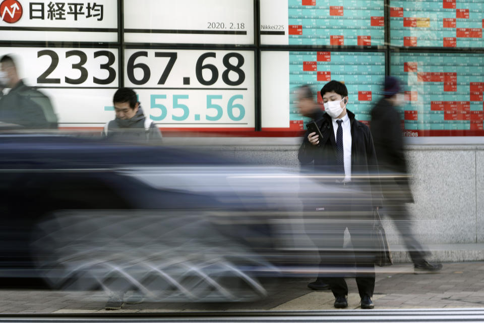 People walk past an electronic stock board showing Japan's Nikkei 225 index at a securities firm in Tokyo Tuesday, Feb. 18, 2020. Shares have fallen in Asia as the impact from the virus outbreak that began in China deepened, with Apple saying it would fail to meet its profit target and China moving to cancel major events including the Beijing auto show. (AP Photo/Eugene Hoshiko)