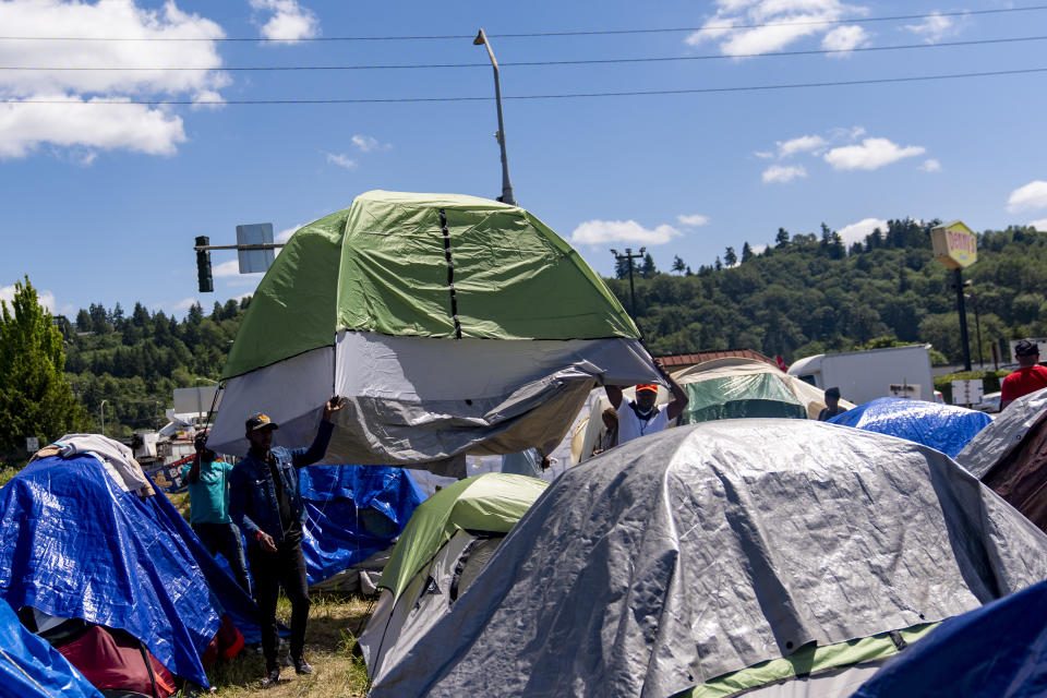 People transport a newly set-up tent at an encampment of asylum-seekers mostly from Venezuela, Congo and Angola next to an unused motel owned by the county, Wednesday, June 5, 2024, in Kent, Washington. The group of about 240 asylum-seekers is asking to use the motel as temporary housing while they look for jobs and longer-term accommodations. (AP Photo/Lindsey Wasson)