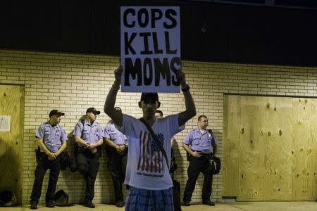 A protester holds a sign aloft in front of police officers before a midnight curfew meant to stem ongoing demonstrations in reaction to the shooting of Michael Brown takes effect in Ferguson, Missouri August 16, 2014. REUTERS/Lucas Jackson