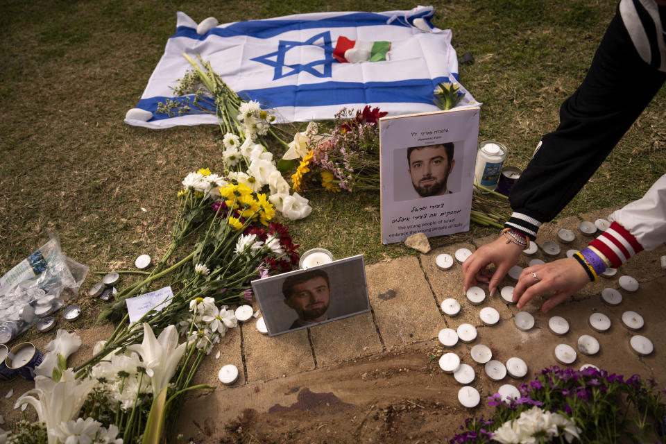 People lay flowers and candles next to photos showing Alessandro Parini, an Italian tourist who was killed in a Palestinian attack, in Tel Aviv, Israel, Saturday, April 8, 2023. Israeli authorities said an Italian tourist was killed and five other Italian and British citizens were wounded Friday when a car rammed into a group of tourists in Tel Aviv. (AP Photo/Oded Balilty)