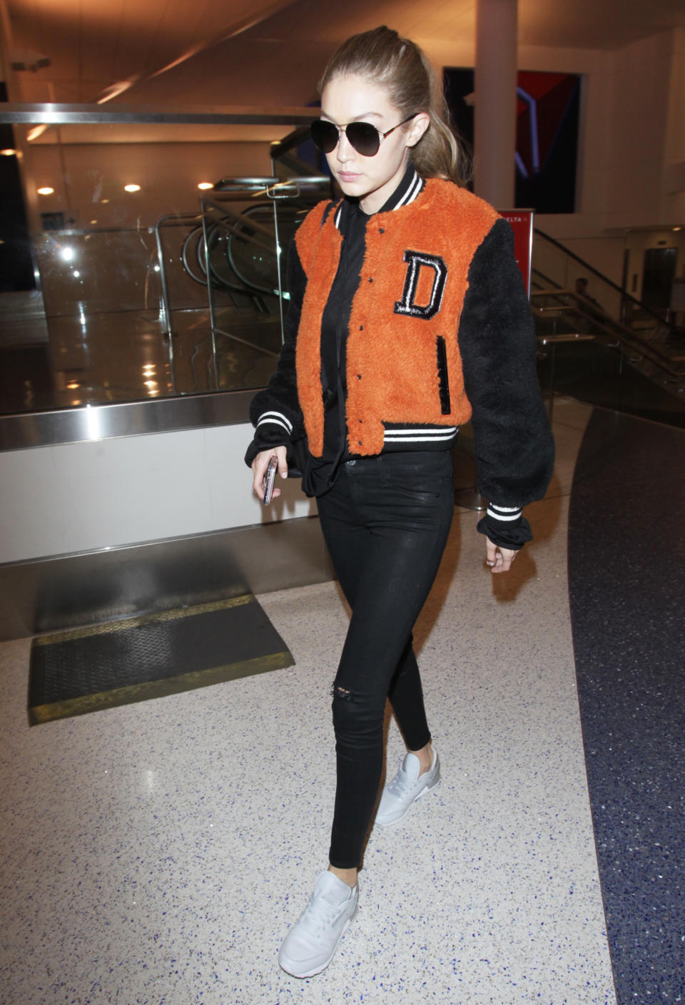<p>Hadid showed off her preppy side in an orange Diesel varsity jacket, black skinny jeans, and white sneakers while catching a flight.</p>