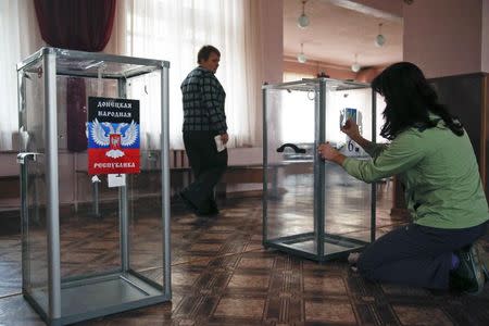 Members of a local electoral commission take part in the preparations for the upcoming election, with a sticker (L) displaying symbols of the self-proclaimed Donetsk People's Republic and the one (R) with the coat of arms of Ukraine seen on ballot boxes, at a polling station in Donetsk, eastern Ukraine, October 31, 2014. REUTERS/Maxim Zmeyev