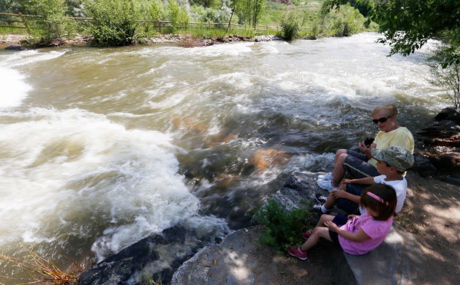 Grandmother sits with her grandchildren as water rushes by in Clear Creek