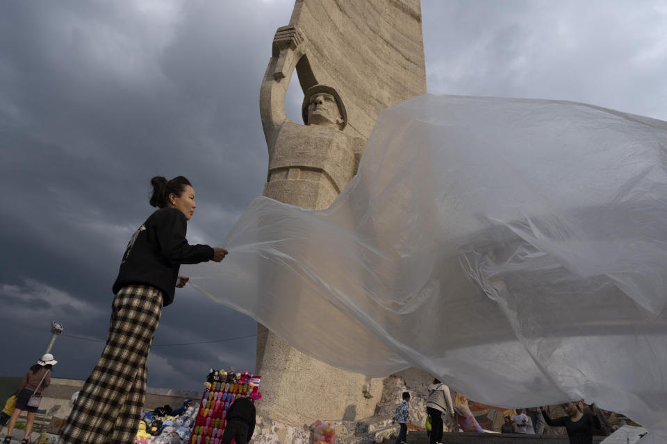 Vendors shake off raindrops from a plastic sheet used to cover prizes for dart games at the Zaisan Memorial, a monument that honors allied Mongolian and Soviet soldiers killed in World War II, in Ulaanbaatar, Mongolia, Saturday, June 29, 2024. (AP Photo/Ng Han Guan)